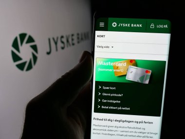 Stuttgart, Almanya - 09-27-2024: Danimarkalı finans şirketi Jyske Bank AS 'in web sayfası ile logo önünde cep telefonu tutan kişi. Telefon ekranının merkezine odaklan.
