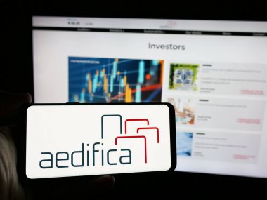 Stuttgart, Almanya - 09-29-2024: Belçikalı emlak şirketi Aedifica SA 'nın logosunu elinde tutan kişi web sitesinin önünde ekranda. Telefon ekranına odaklan.