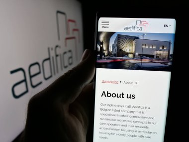 Stuttgart, Almanya - 09-29-2024: Belçikalı emlak şirketi Aedifica SA 'nın web sayfası ile logo önünde cep telefonu tutan kişi. Telefon ekranının merkezine odaklan.