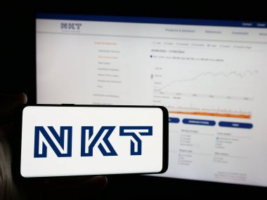Stuttgart, Almanya - 09-29-2024: Üzerinde Danimarkalı voltaj şirketi NKT AS 'nin logosu olan cep telefonu sahibi kişi iş sayfasının önünde ekranda. Telefon ekranına odaklan.