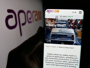 Stuttgart, Germany - 09-29-2024: Person holding cellphone with webpage of steelmaking company Aperam SA on screen in front of logo. Focus on center of phone display. clipart