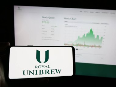Stuttgart, Almanya - 09-29-2024: Danimarkalı bira şirketi Royal Unibrew AS 'in logosunu taşıyan cep telefonu sahibi kişi iş sayfasının önünde ekranda. Telefon ekranına odaklan.