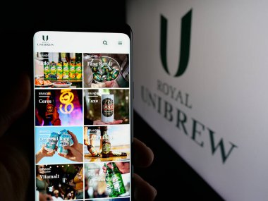 Stuttgart, Almanya - 09-29-2024: Danimarkalı bira şirketi Royal Unibrew AS 'in web sayfası ile cep telefonu tutan kişi logonun önünde ekranda. Telefon ekranının merkezine odaklan.