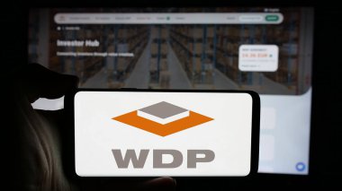 Stuttgart, Germany - 09-29-2024: Person holding cellphone with logo of Belgian company Warehouses De Pauw SA (WDP) on screen in front of business webpage. Focus on phone display. clipart