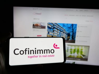 Stuttgart, Almanya - 09-29-2024: Belçikalı emlak şirketi Cofinimmo S.A. 'nın logosunu elinde tutan kişi web sitesinin önünde ekranda. Telefon ekranına odaklan.