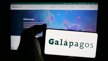 Stuttgart, Germany - 09-29-2024: Person holding smartphone with logo of Belgian pharmaceutical company Galapagos NV on screen in front of website. Focus on phone display. clipart