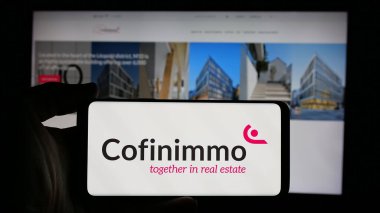 Stuttgart, Almanya - 09-29-2024: Belçikalı emlak şirketi Cofinimmo SA 'nın logosuyla cep telefonu sahibi kişi iş sayfasının önünde ekranda görülüyor. Telefon ekranına odaklan.