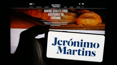 Stuttgart, Almanya - 10-01-2024: Perakende şirketi Jeronimo Martins SGPS SA 'nın logosuyla cep telefonu sahibi kişi iş sayfasının önünde ekranda. Telefon ekranına odaklan.