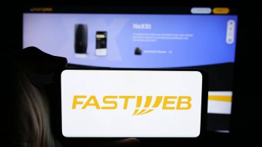 Stuttgart, Almanya - 10-04-2024: Telekomünikasyon şirketi FastWeb S.P.A. logosu olan cep telefonu sahibi kişi iş sayfası önünde ekranda. Telefon ekranına odaklan.