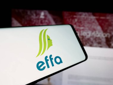 Stuttgart, Germany - 10-04-2024: Mobile phone with logo of European Flavour Association (EFFA) on screen in front of website. Focus on center-left of phone display. clipart