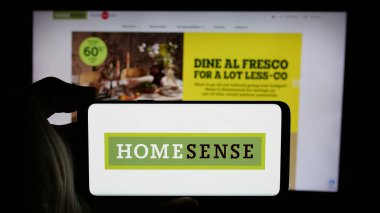 Stuttgart, Almanya - 10-04-2024: Mobilya mağazası şirketi HomeSense 'in logosuyla cep telefonu sahibi kişi iş sayfasının önünde ekranda. Telefon ekranına odaklan.