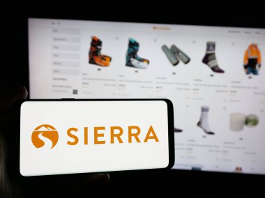 Stuttgart, Almanya - 10-04-2024: Perakende şirketi Sierra Trading Post 'un logosuyla cep telefonu sahibi kişi iş sayfasının önünde ekranda. Telefon ekranına odaklan.