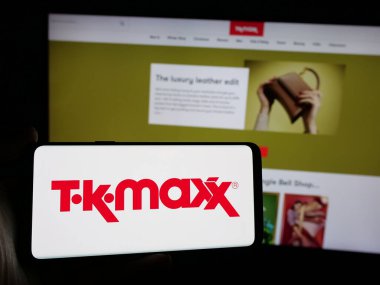 Stuttgart, Almanya - 10-04-2024: Perakende satış şirketi TK Maxx 'in logosuyla cep telefonu sahibi kişi iş sayfasının önünde ekranda. Telefon ekranına odaklan.