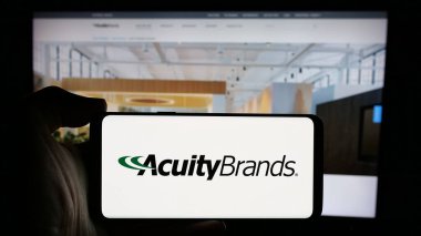 Stuttgart, Almanya - 10-07-2024: ABD 'li ışıklandırma şirketi Acuity Brands Inc.' in logosuyla cep telefonu sahibi kişi iş sayfasının önünde ekranda. Telefon ekranına odaklan.
