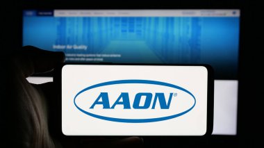 Stuttgart, Almanya - 10-07-2024: Web sitesi önünde ekranda ABD 'li HVAC ekipman şirketi AAON Inc.' nin logosuna sahip akıllı telefonu tutan kişi. Telefon ekranına odaklan.