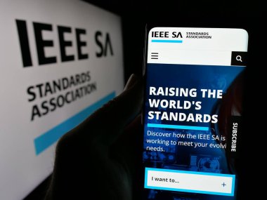 Stuttgart, Almanya - 10-07-2024: Logo önünde ekranda IEEE Standartlar Derneği web sitesi ile cep telefonu tutan kişi. Telefon ekranının merkezine odaklan.
