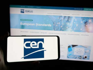 Stuttgart, Almanya - 10-07-2024: İnternet sayfası önünde Avrupa Standartlaştırma Komitesi (CEN) logosu olan cep telefonu sahibi kişi. Telefon ekranına odaklan.