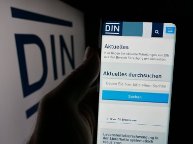 Stuttgart, Almanya - 10-07-2024: Deutsches Institut fuer Normung E.V. web sayfası ile cep telefonu tutan kişi Ekranda logonun önünde. Telefon ekranının merkezine odaklan.