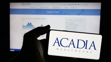 Stuttgart, Almanya - 10-07-2024: ABD 'li Acadia Healthcare Company Inc. şirketinin logosuyla cep telefonu sahibi kişi iş sayfasının önünde ekranda. Telefon ekranına odaklan.