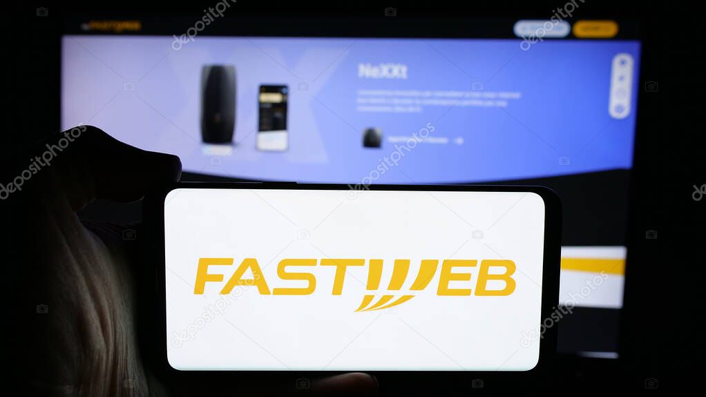 Stuttgart, Germany - 10-04-2024: Person holding cellphone with logo of telecommunications company FastWeb S.p.A. on screen in front of business webpage. Focus on phone display.