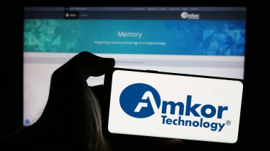 Stuttgart, Almanya - 10-08-2024: Web sayfası önünde ekranda Amerikan yarı iletken şirketi Amkor Technology Inc. 'in logosunu tutan kişi. Telefon ekranına odaklan.