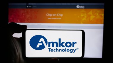 Stuttgart, Almanya - 10-08-2024: İnternet sitesi önünde ekranda, yarı iletken ABD şirketi Amkor Technology Inc. 'in logosuna sahip akıllı telefon sahibi kişi. Telefon ekranına odaklan.