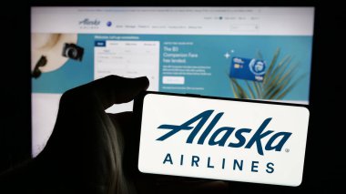 Stuttgart, Almanya - 10-08-2024: ABD 'li havayolu şirketi Alaska Air Group Inc.' in logosuyla akıllı telefon sahibi kişi web sitesinin önünde ekranda. Telefon ekranına odaklan.