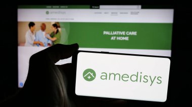 Stuttgart, Almanya - 10-08-2024: ABD 'li sağlık şirketi Amedisys Inc.' in logosuyla cep telefonu sahibi kişi iş sayfasının önünde ekranda. Telefon ekranına odaklan.
