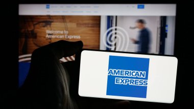 Stuttgart, Almanya - 10-08-2024: İnternet sitesi önünde üzerinde ABD 'li American Express Company (Amex) logosu bulunan akıllı telefon sahibi kişi. Telefon ekranına odaklan.