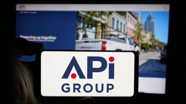 Stuttgart, Almanya - 10-08-2024: ABD 'li iş hizmetleri şirketi APi Group Inc.' nin logosuyla cep telefonu sahibi kişi iş sayfasının önünde ekranda. Telefon ekranına odaklan.