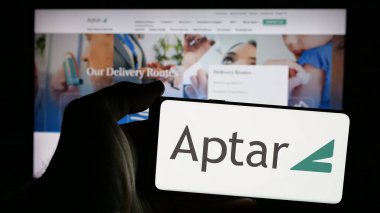 Stuttgart, Almanya - 10-08-2024: İnternet sayfası önünde üzerinde Amerikan ambalaj şirketi AptarGroup Inc. (Aptar) logosu bulunan cep telefonu sahibi kişi. Telefon ekranına odaklan.