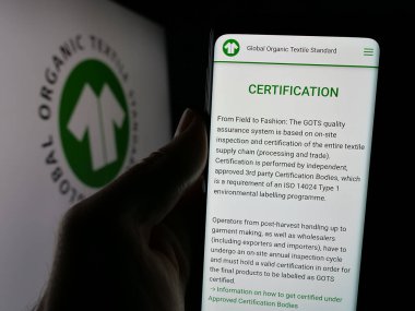 Stuttgart, Almanya - 10-10-2024: Logonun önünde Global Organik Tekstil Standardı (GOTS) web sayfası bulunan kişi. Telefon ekranının merkezine odaklan.