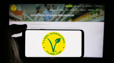 Stuttgart, Almanya - 10-10-2024: İnternet sayfasının önünde EVU sertifikalı V-Label logosu olan cep telefonu sahibi kişi. Telefon ekranına odaklan.