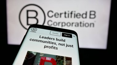 Stuttgart, Germany - 10-10-2024: Mobile phone with website of certification organization B Corporation (B Corp) on screen in front of logo. Focus on top-left of phone display. clipart