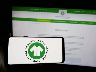 Stuttgart, Almanya - 10-10-2024: Web sitesinin önünde Global Organik Tekstil Standardı (GOTS) logosu olan akıllı telefon sahibi kişi. Telefon ekranına odaklan.