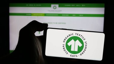 Stuttgart, Almanya - 10-10-2024: Web sayfasının önünde Global Organik Tekstil Standardı (GOTS) logosu olan cep telefonu sahibi kişi. Telefon ekranına odaklan.