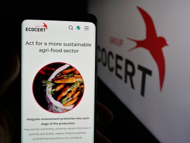 Stuttgart, Almanya - 10-11-2024: Cep telefonunda organik sertifika organizasyonu ECOCERT 'in web sayfası bulunan kişi logolu ekranda. Telefon ekranının merkezine odaklan.