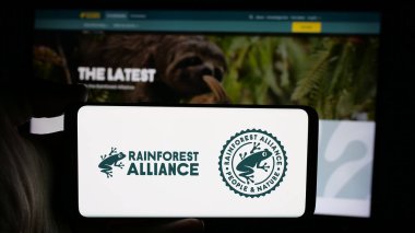 Stuttgart, Almanya - 10-11-2024: İnternet sayfası önünde ekranda Yağmur Ormanları İttifakı organizasyonunun logosuyla cep telefonu tutan kişi. Telefon ekranına odaklan.