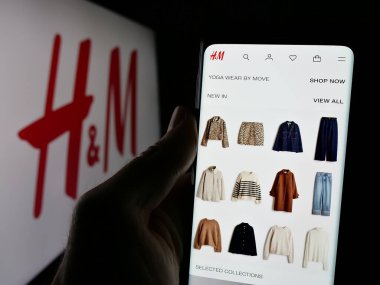 Stuttgart, Almanya - 10-14-2024: İsveçli moda şirketi H ve M 'nin (HM) web sayfası ile logo önünde cep telefonu tutan kişi. Telefon ekranının merkezine odaklan.