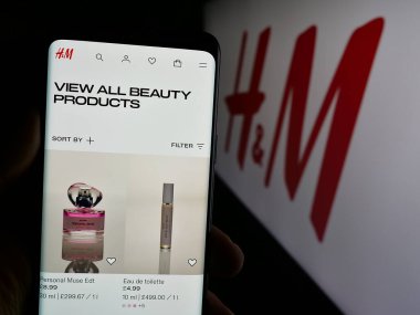 Stuttgart, Almanya - 10-14-2024: İsveçli moda şirketi H ve M 'nin (HM) web sayfası logonun önünde duran kişi. Telefon ekranının merkezine odaklan.