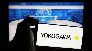 Stuttgart, Almanya - 10-14-2024: Japon şirketi Yokogawa Electric Corporation 'ın logosuna sahip akıllı telefon sahibi kişi web sitesinin önünde ekranda. Telefon ekranına odaklan.