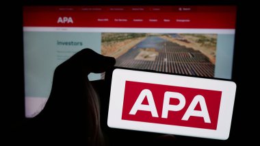 Stuttgart, Almanya - 10-14-2024: Avustralyalı doğalgaz şirketi APA Group 'un logosuyla cep telefonu sahibi olan kişi iş sayfasının önünde ekranda. Telefon ekranına odaklan.