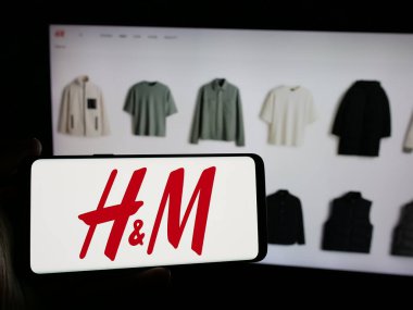 Stuttgart, Almanya - 10-14-2024: İsveçli moda şirketi H ve M 'nin (HM) logosuna sahip cep telefonu sahibi kişi iş sayfasının önünde ekranda. Telefon ekranına odaklan.