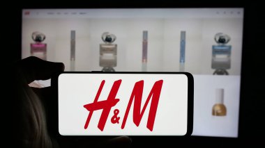 Stuttgart, Almanya - 10-14-2024: İsveçli moda şirketi H ve M 'nin (HM) logosuyla cep telefonu sahibi kişi iş sayfası önünde ekranda. Telefon ekranına odaklan.