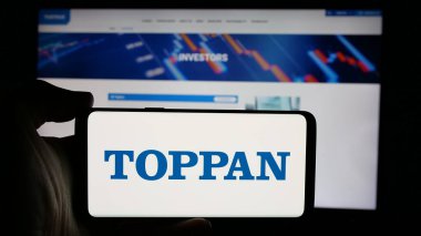 Stuttgart, Almanya - 10-16-2024: Japon şirketi Toppan Holding Inc. 'nin logosuyla cep telefonu sahibi kişi iş sayfasının önünde ekranda. Telefon ekranına odaklan.