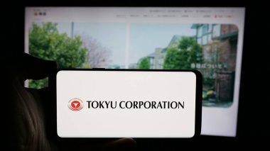 Stuttgart, Almanya - 10-16-2024: Japon holdingi Tokyu Corporation 'ın logosunun bulunduğu cep telefonu sahibi kişi web sayfasının önünde ekranda. Telefon ekranına odaklan.