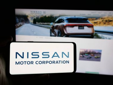 Stuttgart, Almanya - 10-16-2024: Japon şirketi Nissan Motor Corporation 'ın logosunu elinde tutan kişi web sitesinin önünde ekranda. Telefon ekranına odaklan.