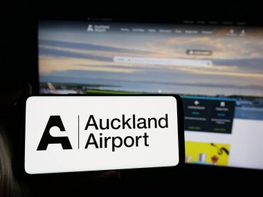 Stuttgart, Almanya - 10-16-2024: Auckland Uluslararası Havalimanı Limited şirketinin logosuna sahip akıllı telefon sahibi kişi web sitesinin önünde ekranda. Telefon ekranına odaklan.