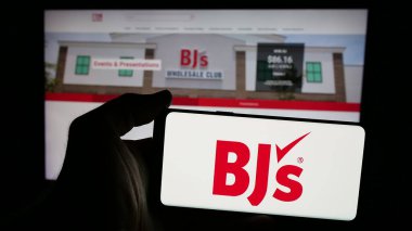 Stuttgart, Almanya - 10-17-2024: Web sitesi önünde ekranda BJ 'in Toptan Kulüp Holding Inc.' sinin logosunu taşıyan kişi. Telefon ekranına odaklan.