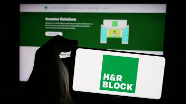 Stuttgart, Almanya - 10-17-2024: İnternet sitesi önünde ekranda ABD vergi hazırlık şirketi HR Block Inc. 'in logosuna sahip akıllı telefonu tutan kişi. Telefon ekranına odaklan.